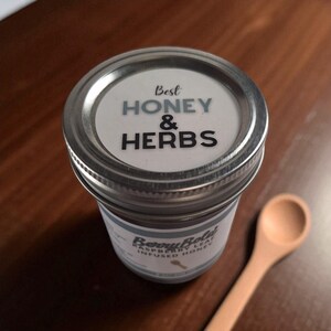 Top view of an 8 oz jar of Raspberry Leaf Honey on a wooden table with a wood spoon.