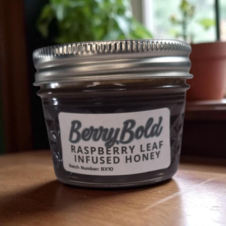 Close-up of 4 oz Raspberry Leaf Infused honey jar with clear label on wood
