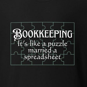 May include: Black t-shirt with the text "BOOKKEEPING It's like a puzzle married a spreadsheet" in a white, puzzle-piece design. The shirt also features a logo for "Southern Canuck Clothing Brand".