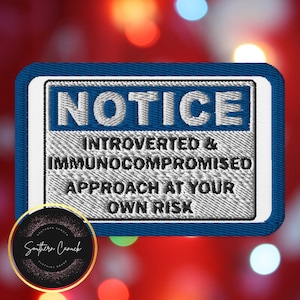 Op de afbeelding: Geborduurde patch met een blauwe rand en het woord "NOTICE" in het wit. De tekst "INTROVERTED & IMMUNOCOMPROMISED APPROACH AT YOUR OWN RISK" staat eronder. Een cirkelvormig logo met tekst staat in de linker benedenhoek.