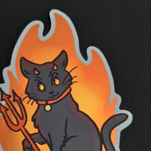 May include: A black cat with red horns and a red trident, sitting in a flame-shaped orange and yellow background.