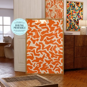 May include: Three digital prints with abstract patterns in orange, white, and blue. The prints are framed in wood and are hanging on a wall in a room with a wooden floor.