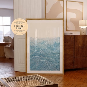 Peut inclure: Une impression encadrée d'une illustration d'ondes océaniques bleues et blanches. L'œuvre est présentée dans un cadre en bois et est appuyée contre un mur. L'impression est intitulée "PHYSICAL PRINT".
