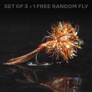 May include: A close-up of a fishing fly with a hook. The fly is made of brown and orange materials with iridescent accents. The text "SET OF 3 + 1 FREE RANDOM FLY" is at the top.