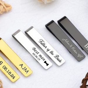 Pode incluir: Uma coleção de clipes de gravata personalizados em ouro, prata e cinza chumbo. Cada clipe é gravado com nomes, iniciais e datas, incluindo "Father of the Bride" e "Best man". Ideal para casamentos e ocasiões especiais.