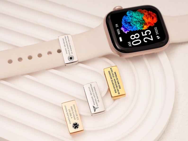 May include: A rose gold smartwatch with a cream strap displays the time and date. Three metal medical alert charms are shown, each with engraved text and a medical symbol. One charm is attached to the watch strap.