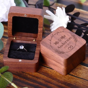 May include: A wooden ring box with a personalized inscription that reads "We decided on forever Mr. & Mrs. Anderson Est. 2023". The box is open and a ring with a single diamond is inside.