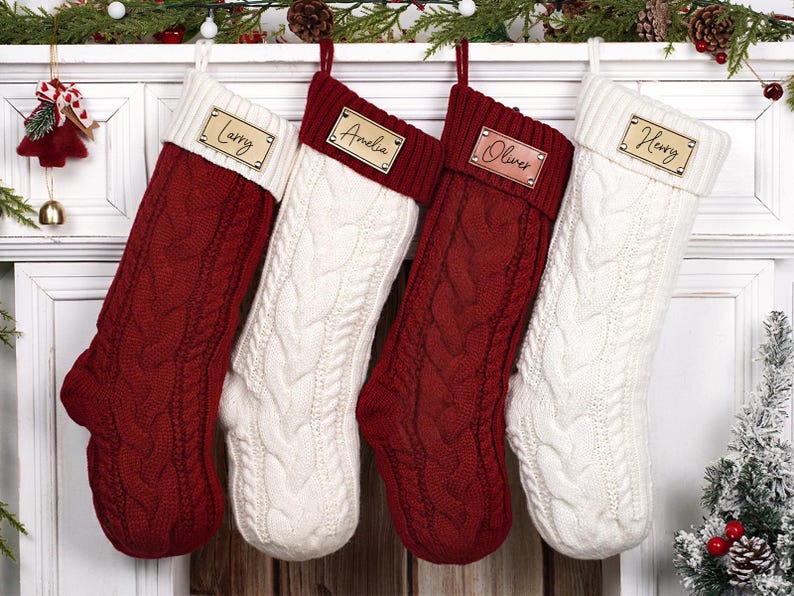 Puede incluir: Cuatro calcetines navide&ntilde;os de punto trenzado cuelgan de una repisa blanca. Dos son rojos, dos son blancos, y cada uno tiene una etiqueta de nombre de madera personalizada. Los nombres son Larry, Amelia, Oliver y Henry. Decoraci&oacute;n festiva.