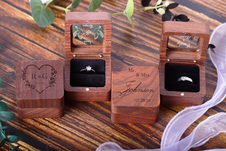 May include: Three wooden ring boxes with different engravings. The first box has a heart with the initials R&G and the words "Forever Yours". The second box has a pair of doves with the words "Forever Yours". The third box has the text "Mr. & Mrs. Johnson 07.28.24".