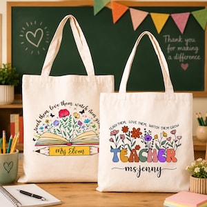 May include: Two off-white canvas tote bags featuring colorful floral designs and the text "Teach them, love them, watch them grow." The left bag includes a book and pencil graphic with "Mrs Elven," while the right bag features the word "TEACHER" and "ms jenny."