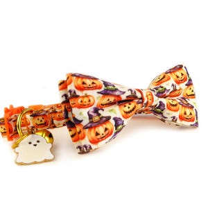 May include: A Halloween-themed pet collar and bow tie set. The white fabric is patterned with orange jack-o'-lanterns wearing witch hats. The collar has an orange buckle and a ghost-shaped charm. A festive accessory for pets.