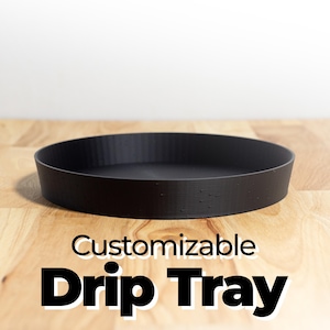 May include: A black, round, customizable drip tray. The tray is made of a smooth, matte material and has a slightly raised lip around the edge.