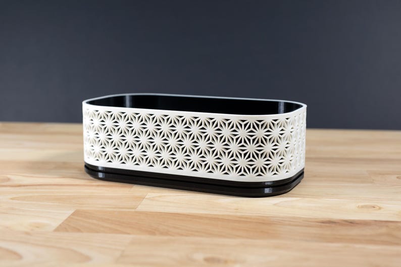 Op de afbeelding: Een rechthoekige opbergcontainer met een geometrisch sterrenpatroon. De container is wit met een zwart interieur en basis. De container is ongeveer 20 cm lang, 10 cm breed en 8 cm hoog.