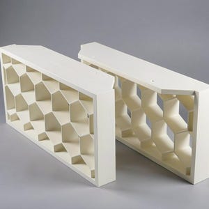 May include: Two off-white, geometric shelves with a honeycomb design. Each shelf is rectangular with a series of hexagonal openings. The shelves are made of a solid material and are suitable for displaying items.