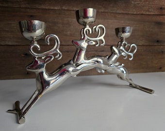 May include: Silver reindeer candle holder with three candle cups. The reindeer are leaping and their antlers are intertwined.