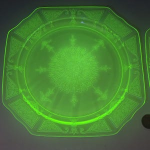 May include: Two octagonal, neon green glass plates with an etched design. The plates have a vintage aesthetic, with a glowing appearance. Each plate features an ornate design around the rim and a central sunburst pattern. The plates are a vibrant, eye-catching addition.