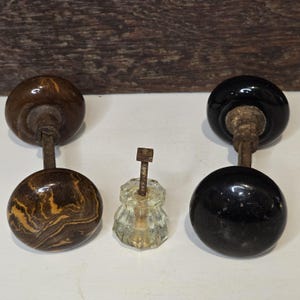 May include: Three antique door knobs, two with black glass and one with brown marbled glass. The knobs are attached to metal stems.