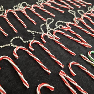 Puede incluir: Una cadena de adornos de bastón de caramelo rojo y blanco con detalles de cuentas transparentes. Los bastones de caramelo cuelgan de una cuerda transparente.