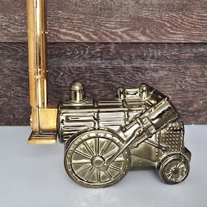 May include: A gold-coloured, decorative model of a vintage steam engine. The model features a tall smokestack, detailed wheels, and intricate mechanical components, set against a wooden background. The train is a detailed replica of a classic locomotive.