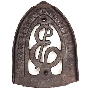 May include: Antique cast iron Enterprise Mfg. Co. flat iron base. The iron base is dark brown with the company name and logo etched into the metal. The base has a decorative openwork design with the letters "E" and "C".