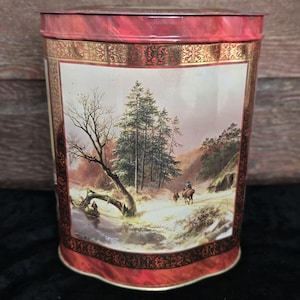 May include: A red metal tin with a gold trim and a winter scene with trees and people on horseback. The tin has a marbled red finish.