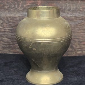 May include: A brass vase with a rounded body and a flared base. The vase has a subtle, aged patina and a decorative band around the middle.