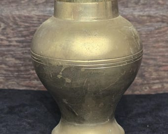 May include: A brass vase with a rounded body and a flared base. The vase has a subtle, aged patina and a decorative band around the middle.
