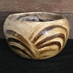 May include: A brown and cream ceramic planter with a wavy, abstract design. The planter has a wide, round opening and a slightly rounded bottom.