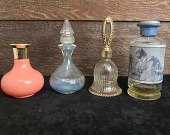 May include: Four vintage perfume bottles with different shapes and colours. The bottles are arranged in a row on a black surface. The bottles are made of glass and have gold accents. The bottles are all different sizes and shapes.