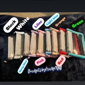 May include: Clear zip binders in various colors including black, white, lilac, light blue, orange, green, pink, and navy blue. The text "Inventory is updated on my site!" is displayed at the top. The text "ZIP BINDERS" is at the bottom.
