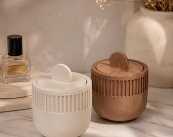 May include: Two cylindrical containers with lids, one in off-white and one in a warm brown tone. Each container features a vertical ribbed texture around the upper body and a circular handle on the flat lid. The containers have a smooth finish.