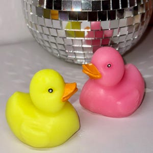 May include: Two rubber duck bath toys, one yellow and one pink. The yellow duck has an orange beak and black eyes. The pink duck has an orange beak and black eyes.