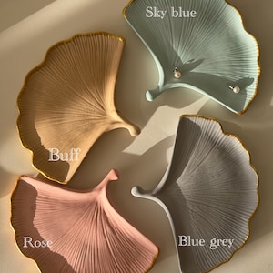 Op de afbeelding: Vier keramische ginkgo-bladschalen in verschillende kleuren: buff, roze, hemelsblauw en blauwgrijs. Elke schaal heeft een gouden rand.