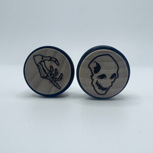 May include: Two round wooden coasters with black and white designs. One coaster features a skeleton hand, the other features a skull.