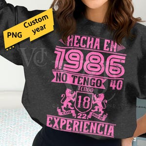 Könnte beinhalten: Dunkelgraues Sweatshirt mit einem rosa Aufdruck mit der Aufschrift "HECHA EN 1986" und "NO TENGO 40 TENGO 18 CON 22 AÑOS DE EXPERIENCIA". Ein gelber "Custom year PNG" Aufkleber befindet sich in der oberen linken Ecke.