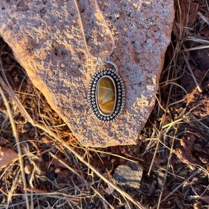 May include: A silver pendant necklace with a brown and white agate stone set in a silver bezel. The pendant is surrounded by a row of silver beads.
