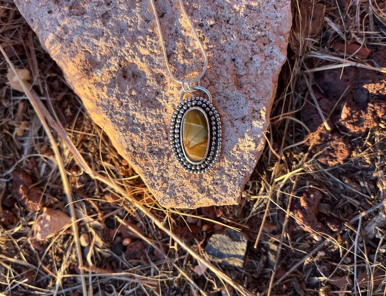 May include: A silver pendant necklace with a brown and white agate stone set in a silver bezel. The pendant is surrounded by a row of silver beads.