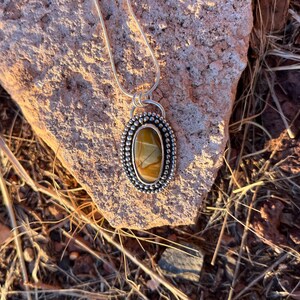 May include: A silver pendant necklace with a brown and yellow agate stone set in a silver bezel. The stone has a unique pattern and is surrounded by small silver beads.