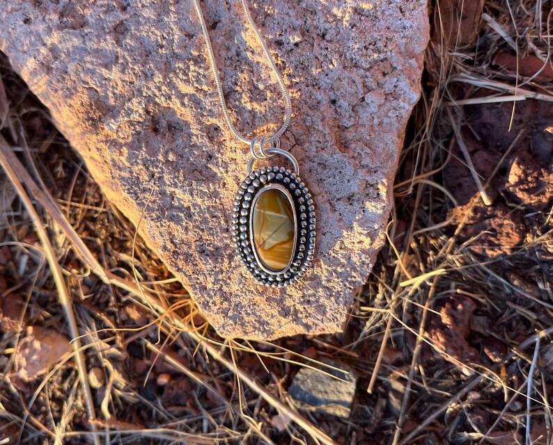 May include: A silver pendant necklace with a brown and yellow agate stone set in a silver bezel. The stone has a unique pattern and is surrounded by small silver beads.