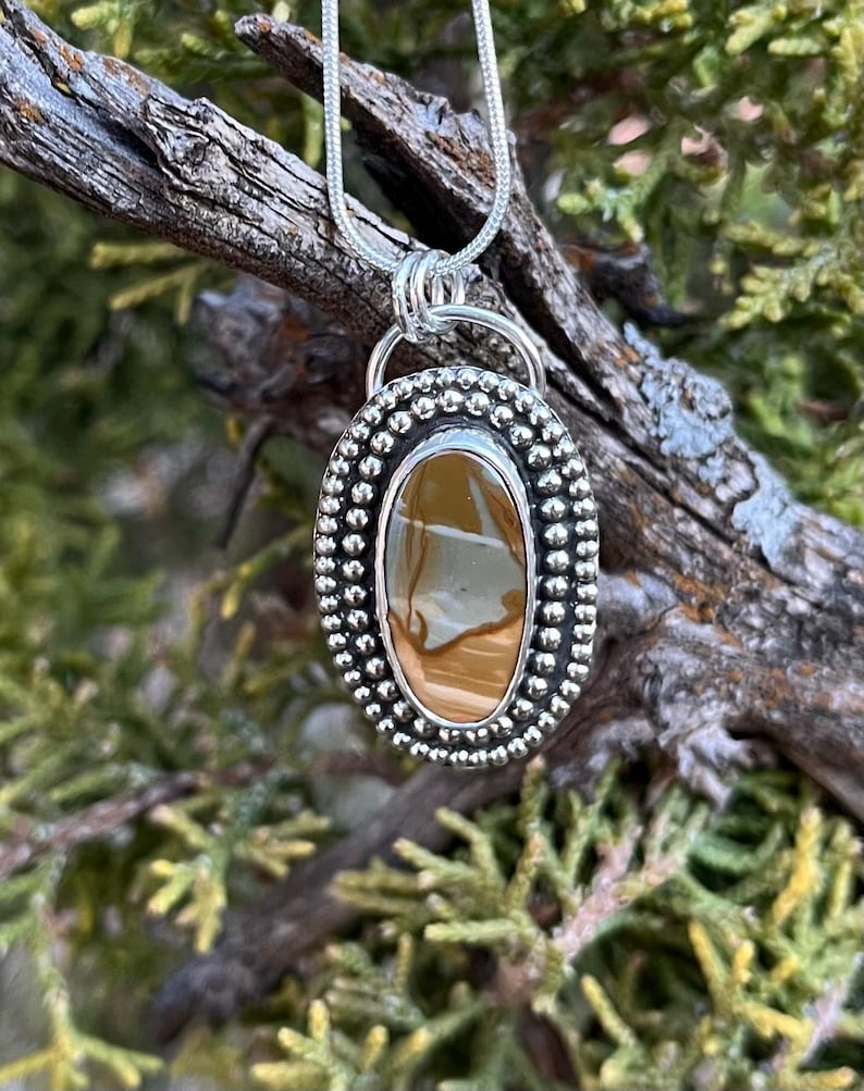 May include: A silver pendant with a brown and white agate stone set in a beaded oval frame. The pendant is hanging from a silver chain.