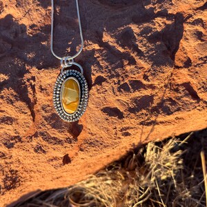 May include: A silver chain necklace with a pendant featuring a yellow and brown agate stone set in a silver bezel with a beaded border.