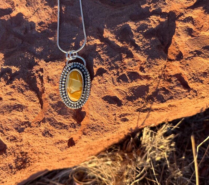 May include: A silver chain necklace with a pendant featuring a yellow and brown agate stone set in a silver bezel with a beaded border.