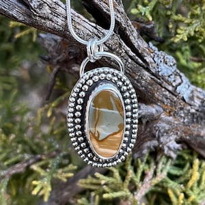 May include: A silver pendant with a brown and white agate stone set in a beaded oval frame. The pendant is hanging from a silver chain.