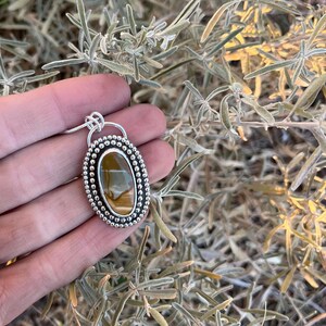 May include: A silver pendant with a brown and gold tiger's eye stone set in a beaded oval frame.