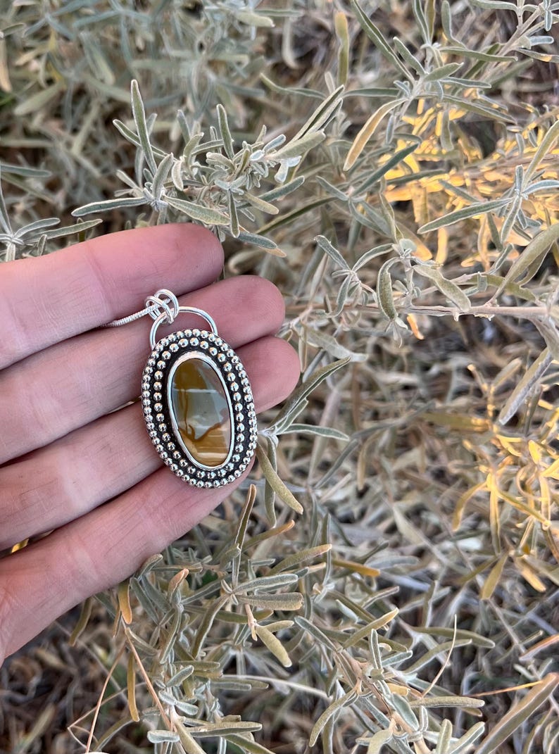 May include: A silver pendant with a brown and gold tiger's eye stone set in a beaded oval frame.