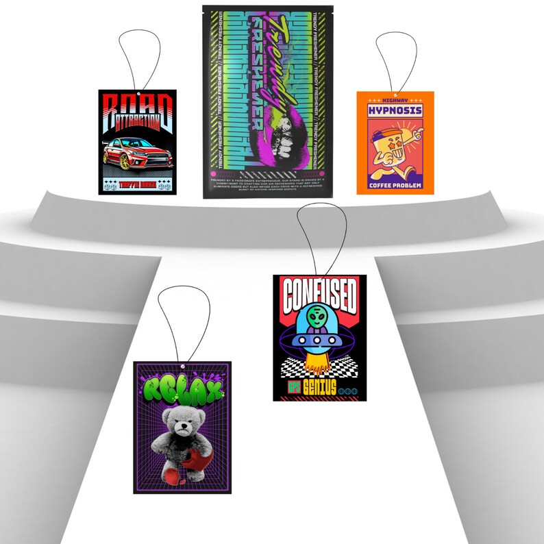 May include: Four car air fresheners with different designs. The first is black with a red car and the text "Road Attraction". The second is black with a pink and green design and the text "Trendy Freshener". The third is orange with a cartoon character and the text "Highway Hypnosis Coffee Problem". The fourth is black with a UFO and the text "Confused Off Genius".