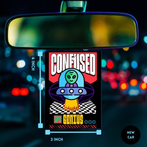 May include: A black and red car air freshener with a cartoon alien in a spaceship. The text "CONFUSED" is in red and "GPS GENIUS" is in green. The air freshener is 3 inches wide and 4 inches tall.
