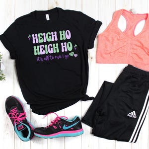 May include: Black t-shirt with the text "Heigh Ho Heigh Ho it's off to run I go" in green and purple lettering with pink glitter accents. The shirt is paired with black athletic pants, a pink sports bra, and pink and black running shoes.