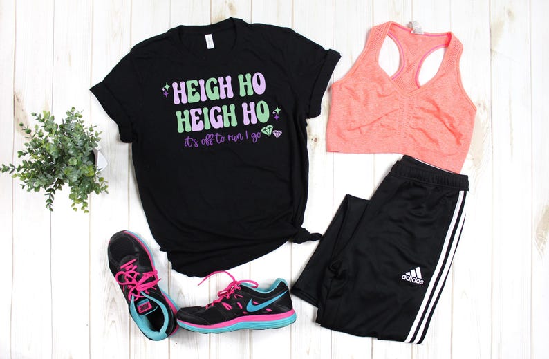 May include: Black t-shirt with the text "Heigh Ho Heigh Ho it's off to run I go" in green and purple lettering with pink glitter accents. The shirt is paired with black athletic pants, a pink sports bra, and pink and black running shoes.