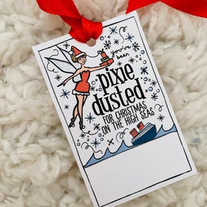 Peut inclure: Une étiquette cadeau blanche avec une illustration de fée de dessin animé avec des ailes rouges et une robe rouge tenant une boîte cadeau. Le texte sur l'étiquette dit "You've been pixie dusted for Christmas on the high seas".